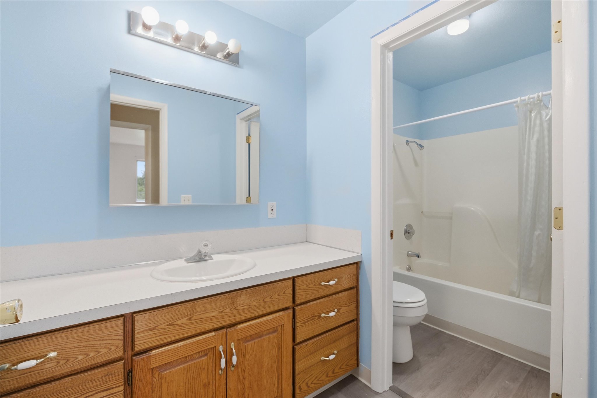 Bathroom featuring a white single-basin vanity with a wood-finish cabinet, a large mirror, and a chrome light fixture