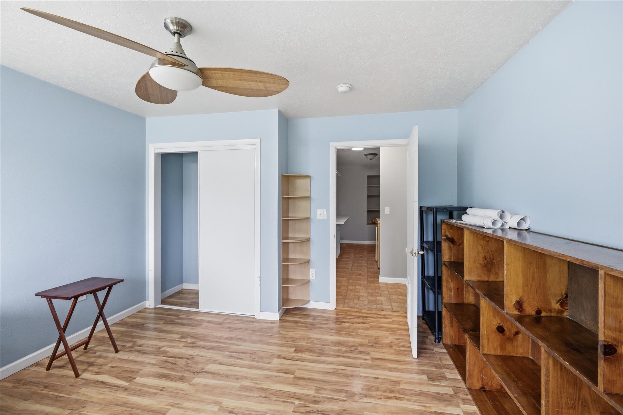 Room featuring wood-finish flooring, light blue wall paint, and a ceiling fan with integrated lighting