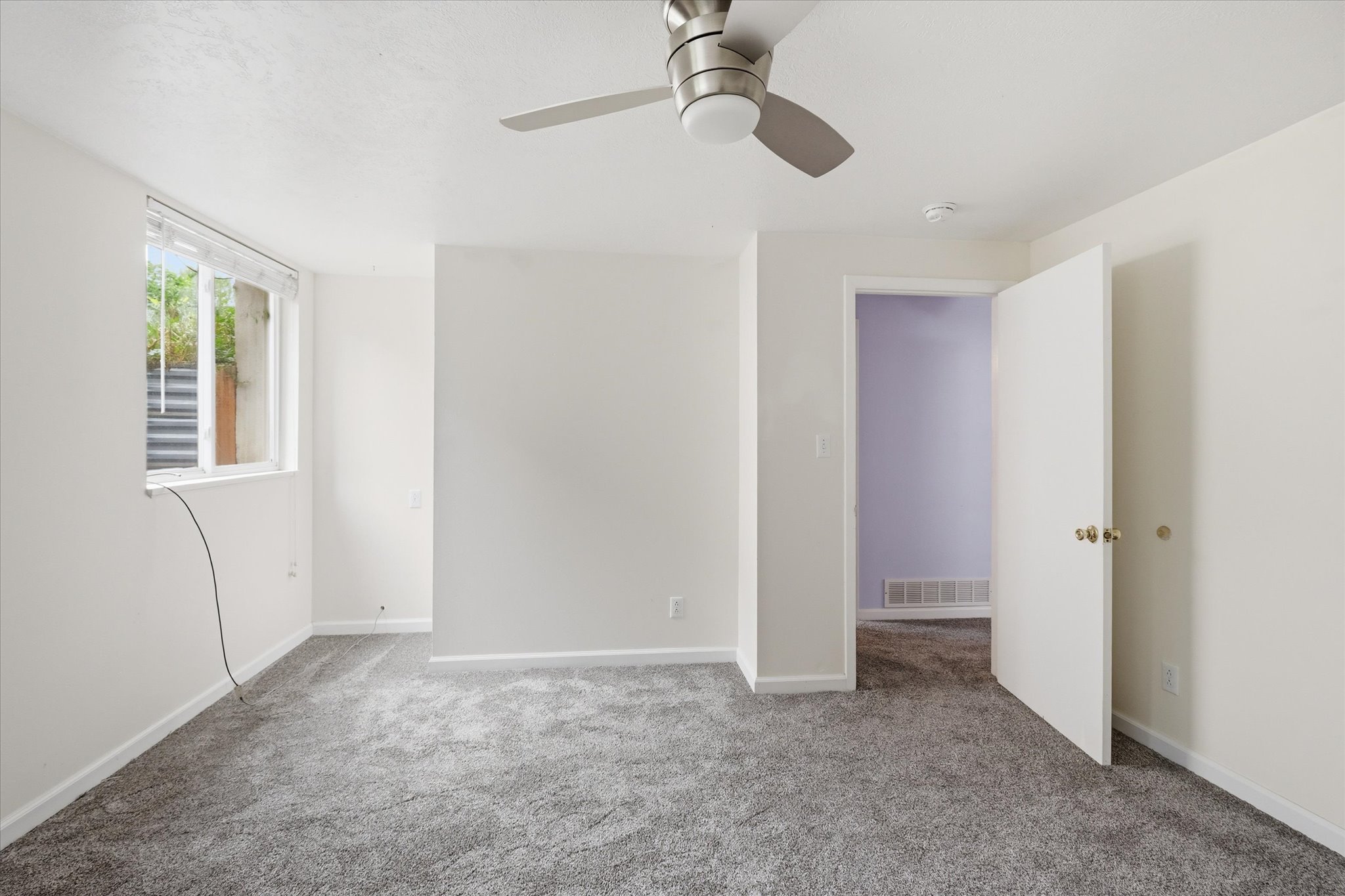 Room featuring grey carpeting, white walls, a ceiling fan with integrated lighting, and a white-framed window