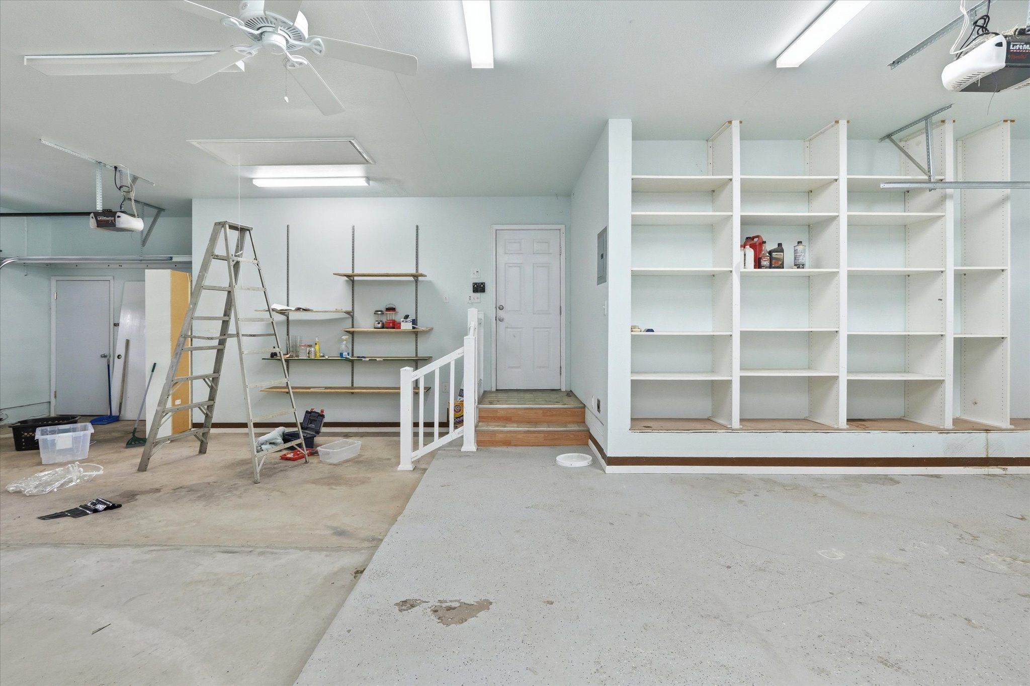 Spacious garage featuring a concrete floor, built-in shelving, two ceiling fans, fluorescent lighting, and a service door
