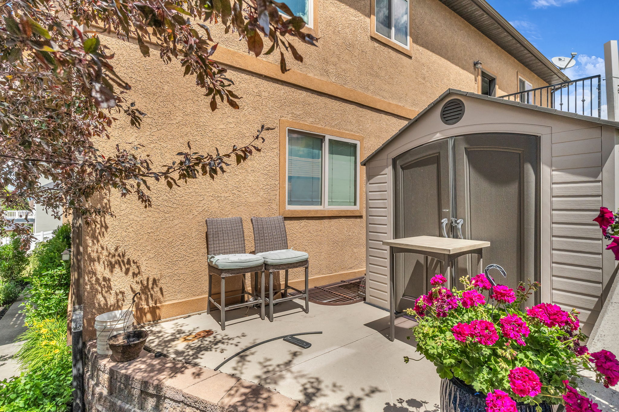 Stucco exterior featuring a hardscaped patio, an integrated storage shed, and a privacy wall