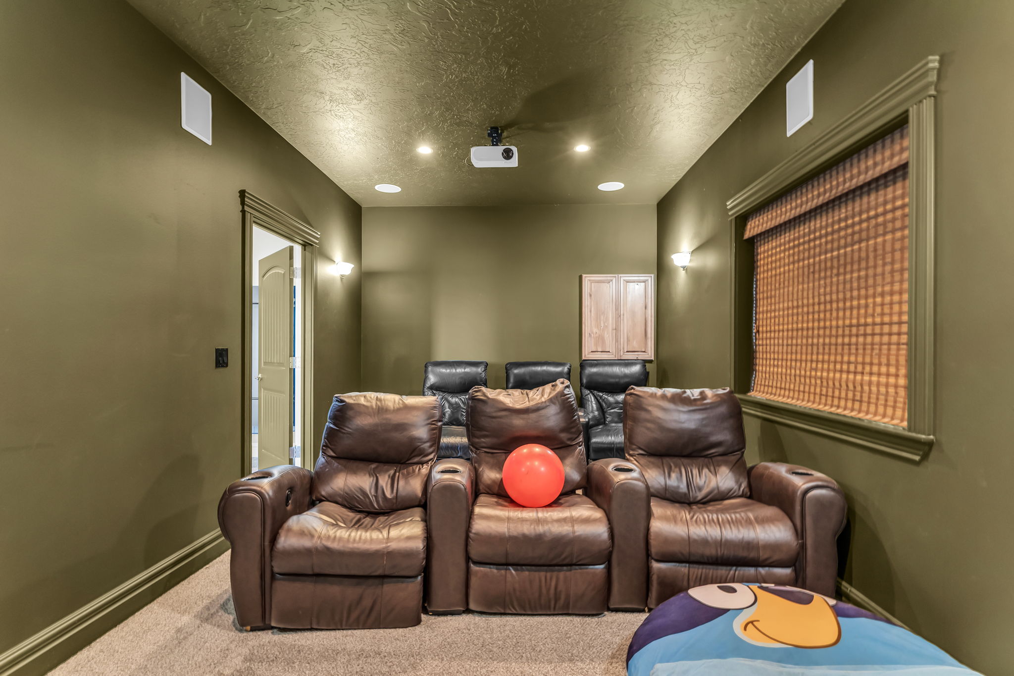 Dedicated media room featuring recessed lighting, wall sconces, integrated ceiling speakers, and a ceiling-mounted projector