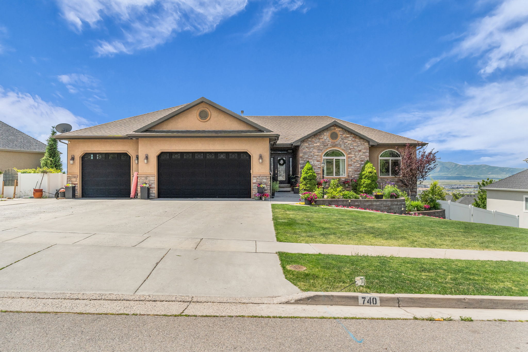 Split-level residence featuring a two-car garage with black doors and exterior sconces, a stone facade, and arched windows