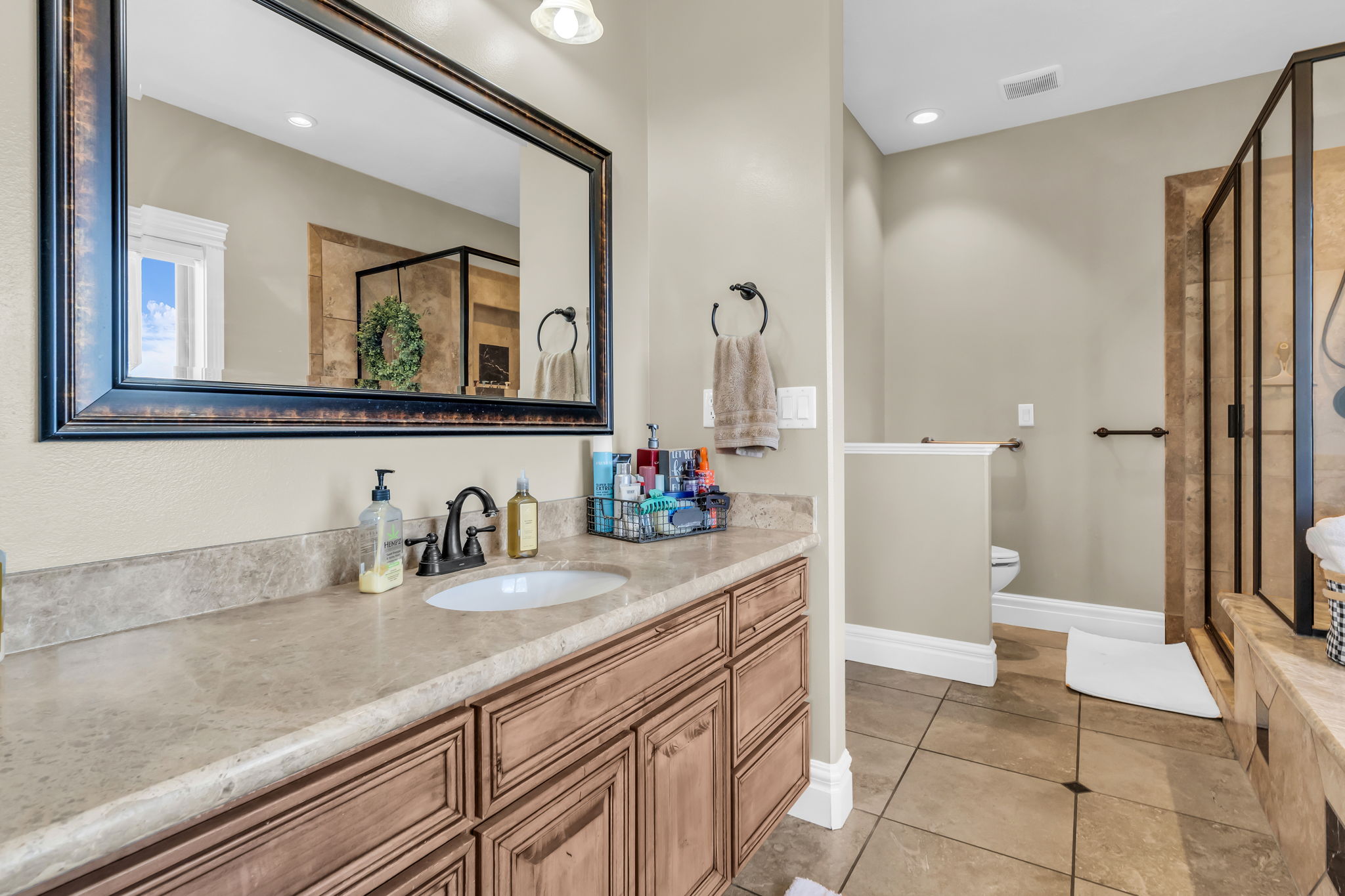 Bathroom featuring a vanity with a light-toned countertop and an integrated sink, a framed mirror, and a glass-enclosed shower with tile surround