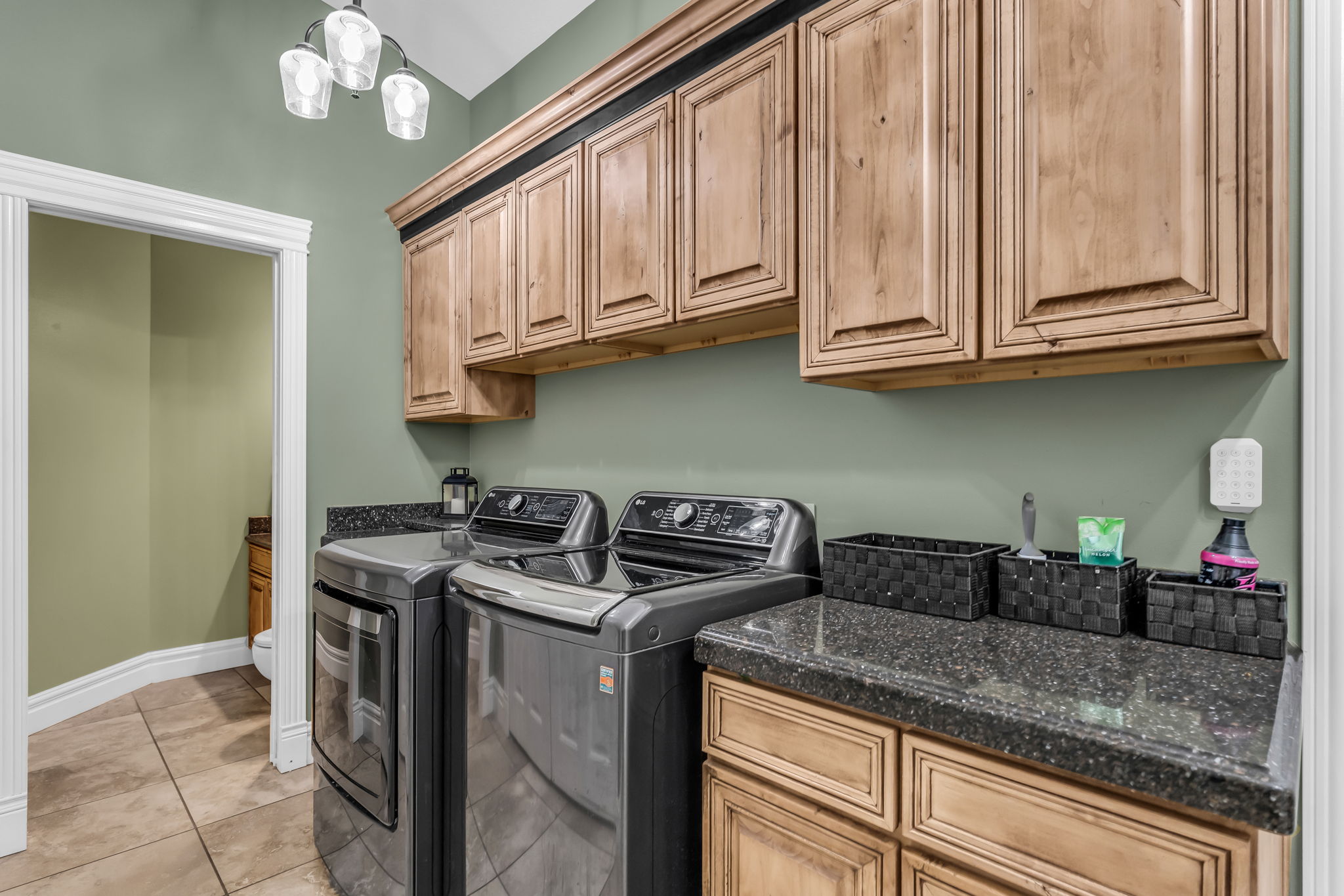 Laundry area featuring extensive upper and lower wood cabinetry, dark speckled countertops, and tile flooring