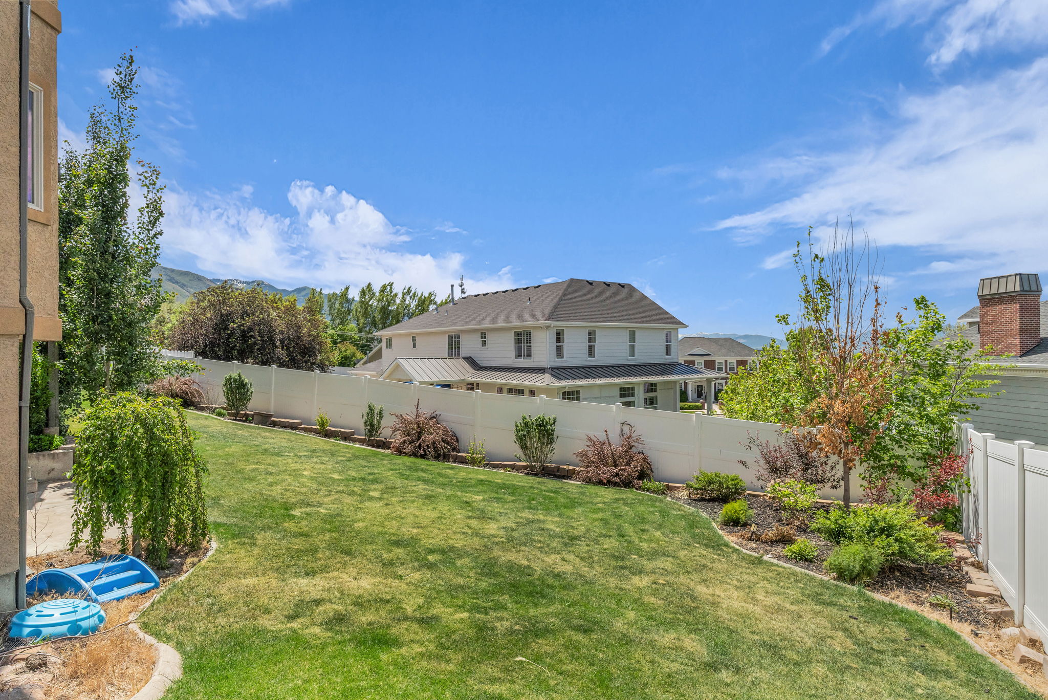 Expansive backyard featuring a manicured lawn, established landscaping, and a white privacy fence