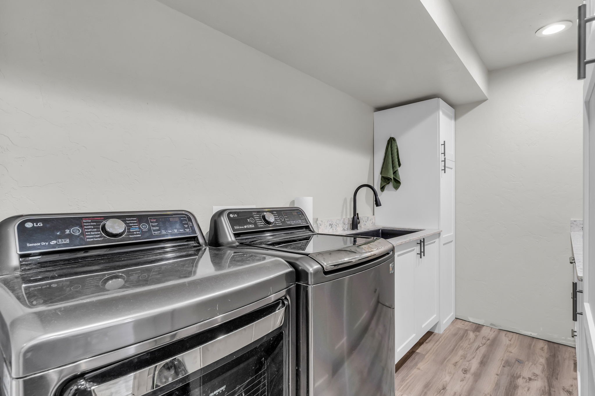 Laundry room featuring white cabinetry, a built-in sink with a black faucet, wood-finish flooring, and recessed lighting