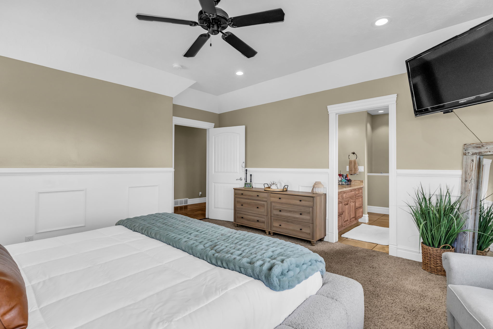 Carpeted bedroom featuring wainscoting, a tray ceiling, and a ceiling fan with integrated lighting