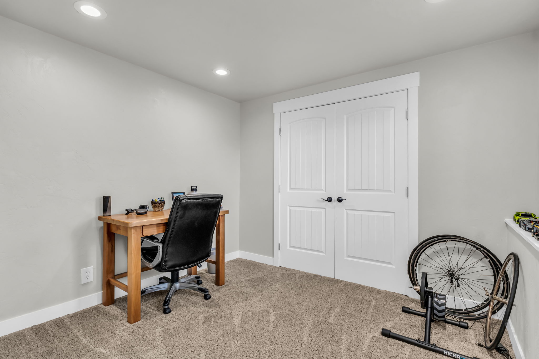 Recessed lighting illuminates a space featuring light gray walls, plush carpet flooring, and white baseboards