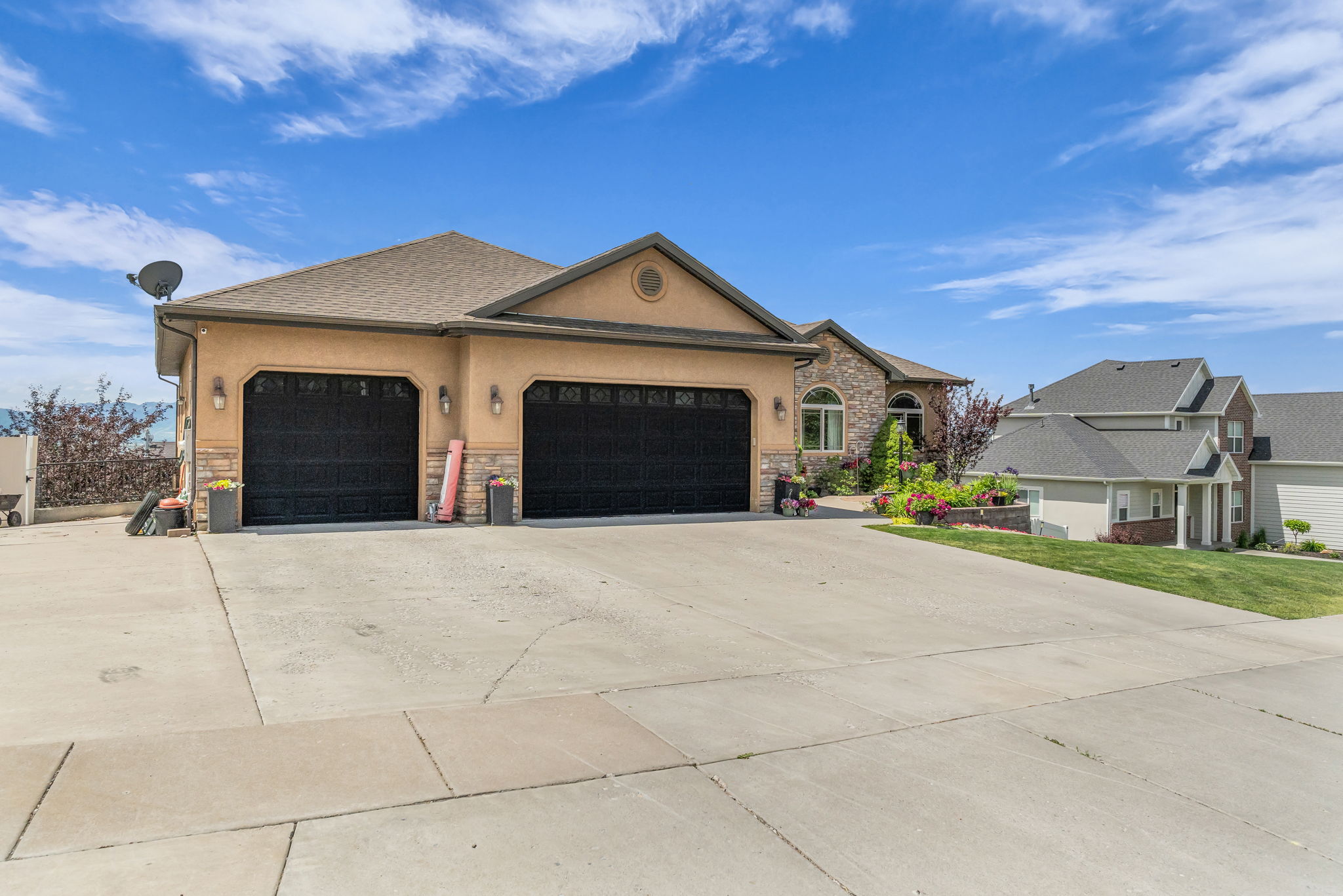 Stucco and stone exterior with a two-car garage, concrete driveway, arched entryway, and mature landscaping