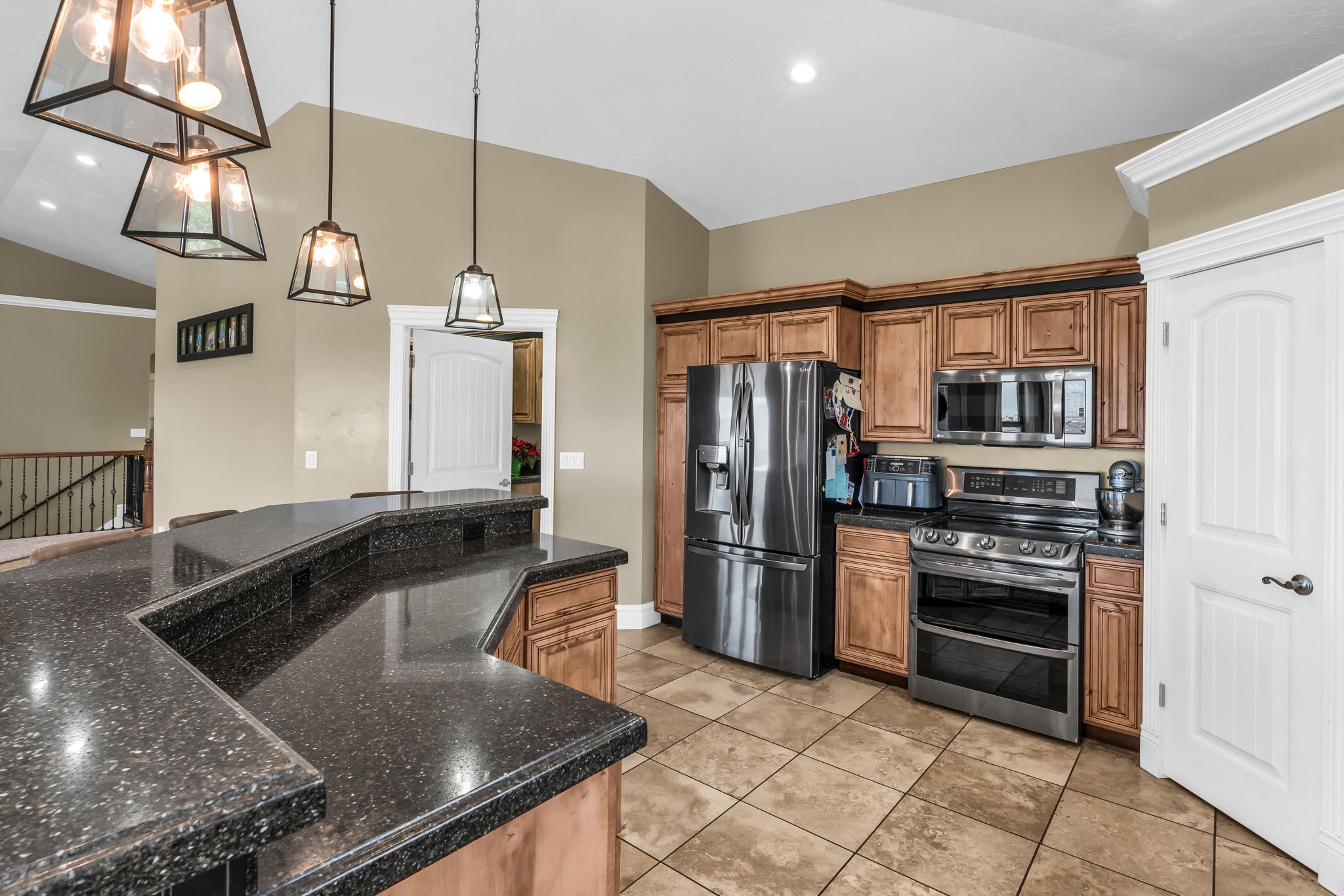 Kitchen featuring a multi-level breakfast bar with speckled countertops, wood-finish cabinetry, stainless steel appliances, and recessed lighting