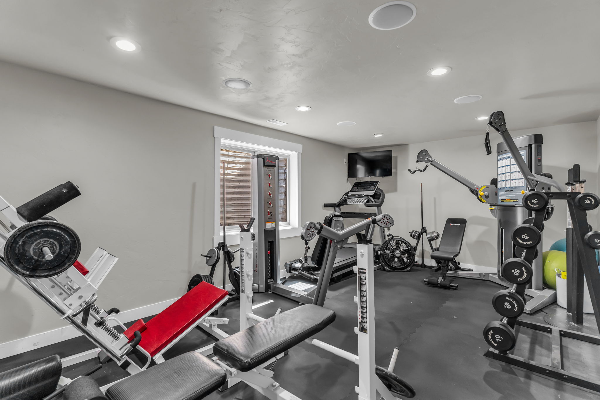 Dedicated fitness room featuring recessed lighting, a window with horizontal blinds, and dark rubberized flooring