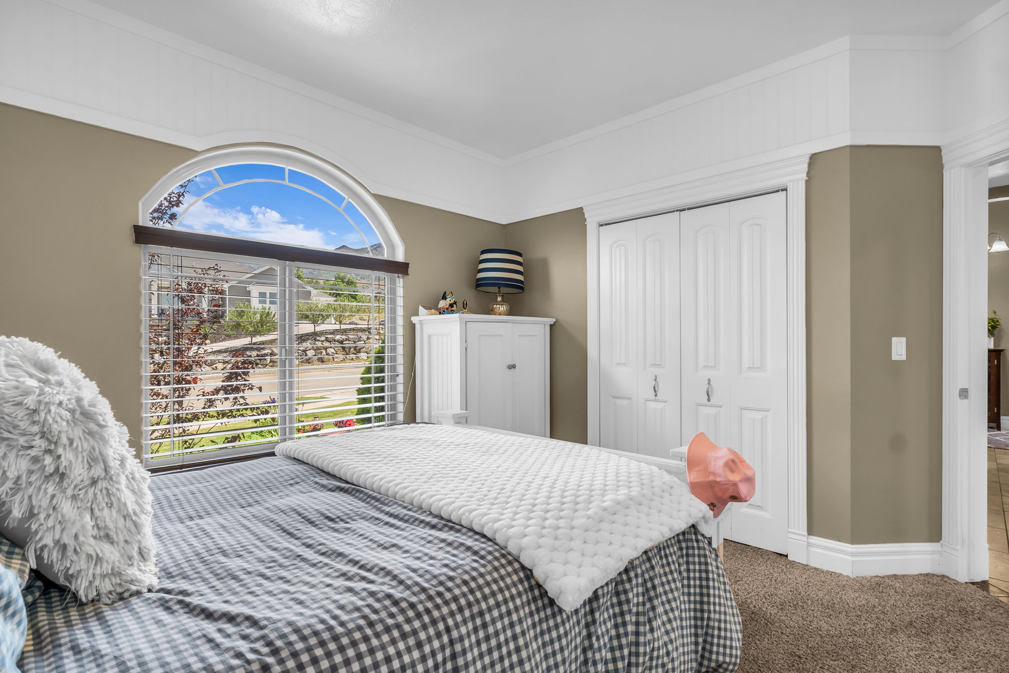 Room featuring an arched window with louvered blinds, crown molding, bifold closet doors, and carpet flooring