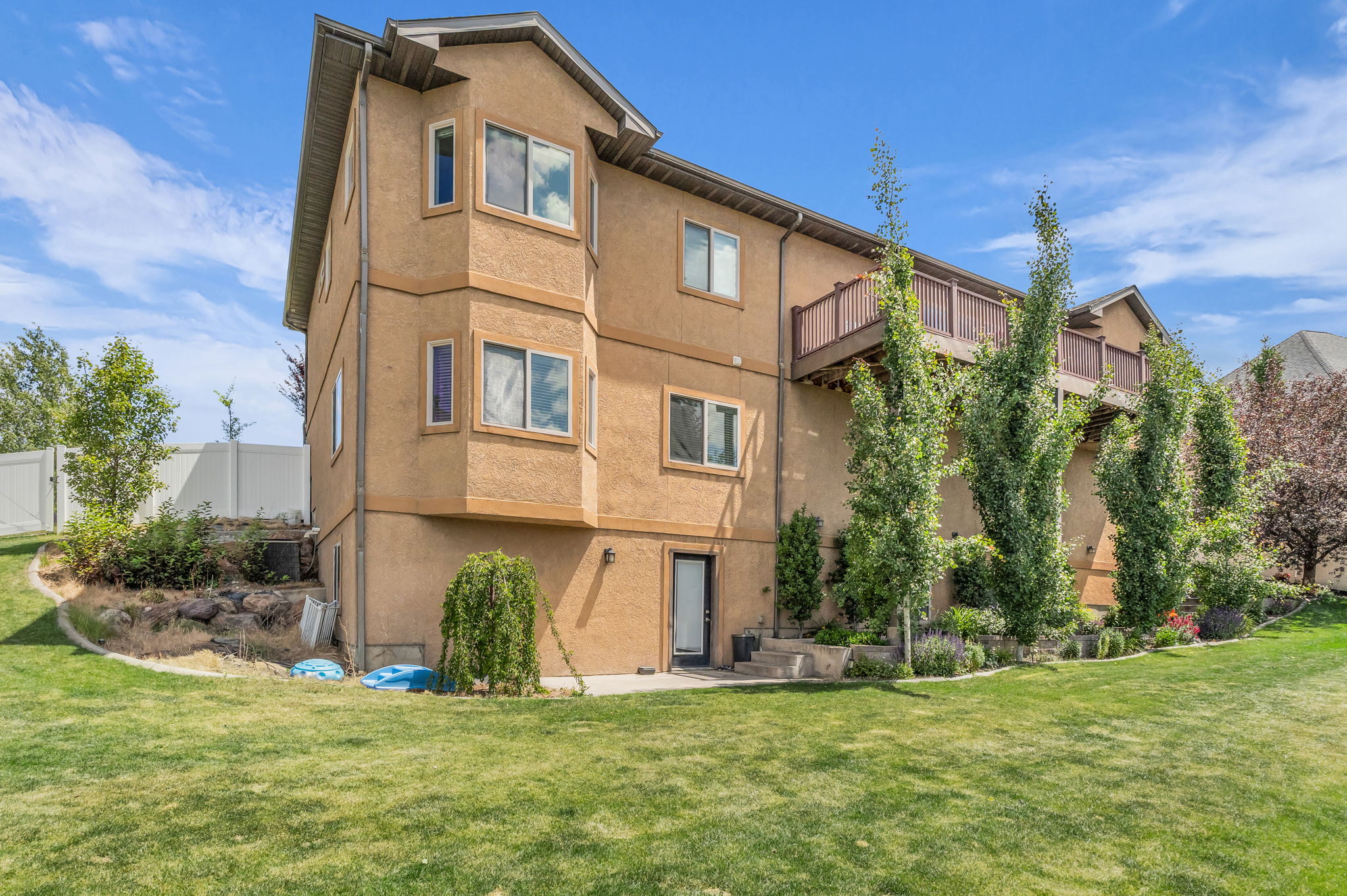 Spacious rear yard featuring an expansive lawn, mature trees, and a multi-level stucco exterior