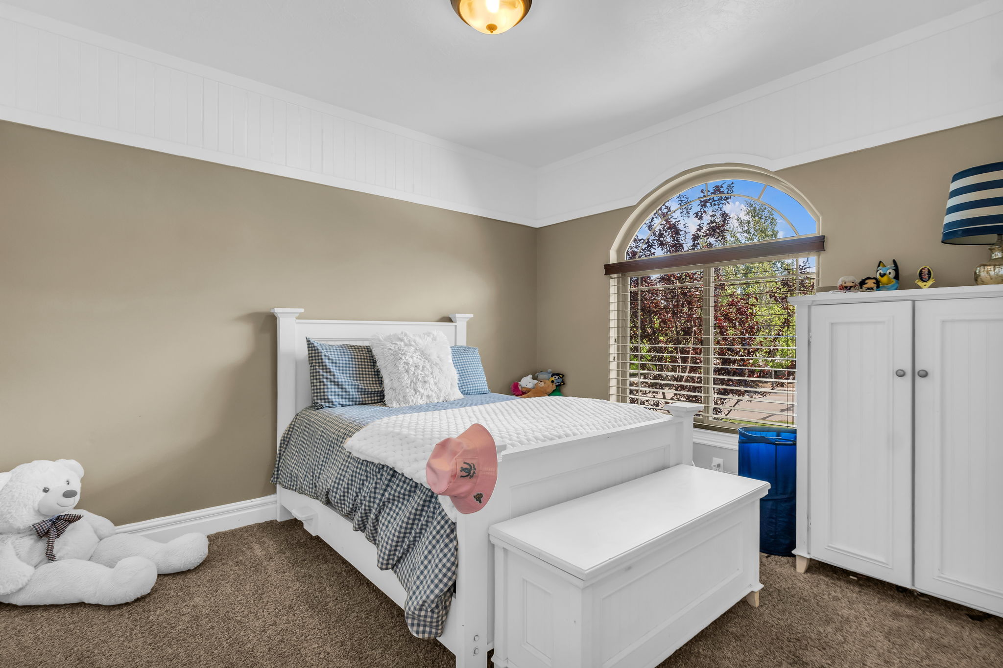 Carpeted room featuring a large arched window with blinds, a built-in wall cabinet, and crown molding