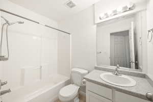 Bathroom featuring a white bathtub with a tiled surround, a white toilet, a vanity with a light-toned countertop, an oval undermount sink, and a mirrored wall cabinet with integrated lighting