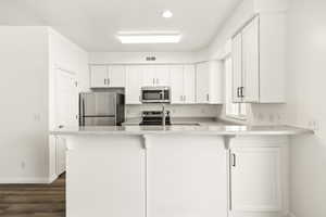Kitchen featuring white cabinetry, stainless steel appliances, speckled countertops, and wood-finish flooring