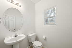 Pedestal sink with chrome faucet, complemented by a round mirror and a three-light vanity fixture