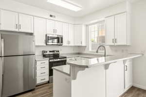 Bright kitchen featuring white cabinetry, stainless steel appliances, speckled countertops, wood-finish flooring, and a breakfast bar