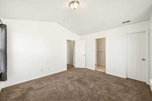 Carpeted interior space featuring vaulted ceilings and a flush-mount ceiling light fixture