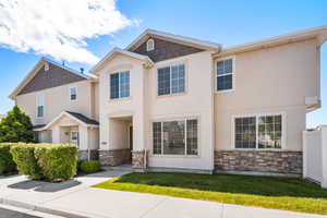 Two-story residence featuring stucco and stone veneer facade, gabled rooflines with shake-style siding, multiple windows with grilles, a covered entryway, and a white privacy fence