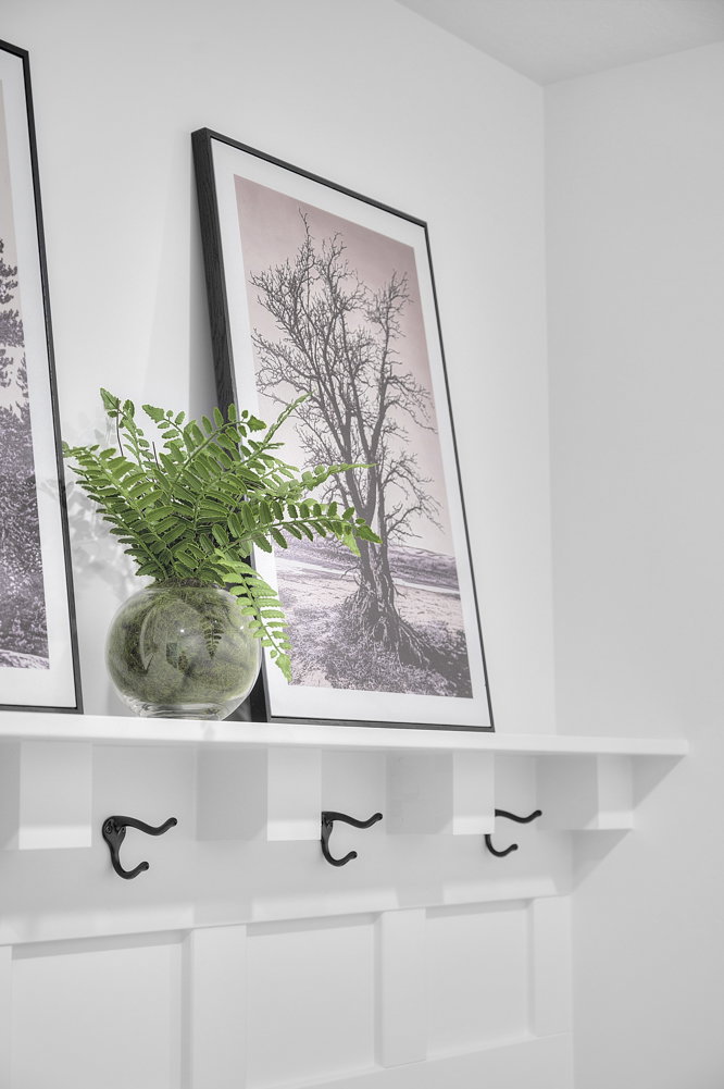 Built-in white shelving unit with three matte black coat hooks and paneled wainscoting