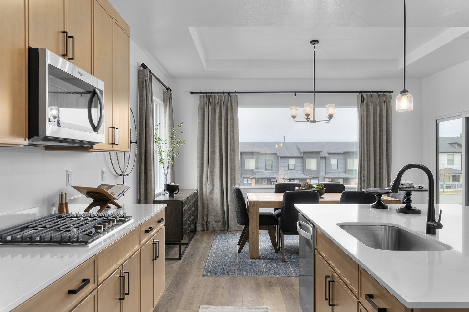 Open-concept kitchen and dining area with wood-finish flooring, light wood cabinetry, white countertops, and stainless steel appliances