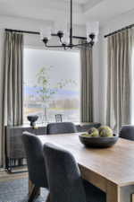 Dining area featuring a wood-finish table, upholstered chairs, and a black chandelier with clear glass shades