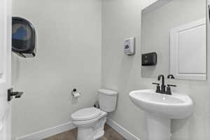 White pedestal sink with matte black faucet, wall-mounted mirror, white commode, and wood-finish flooring