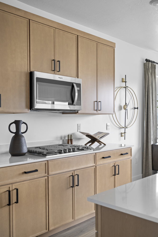 Kitchen featuring light wood-finish cabinetry with black hardware, a built-in stainless steel microwave, a gas cooktop, and light-toned countertops