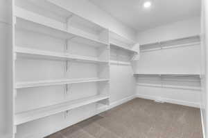 Spacious walk-in closet featuring extensive built-in shelving, multiple hanging rods, recessed ceiling lighting, and carpet flooring