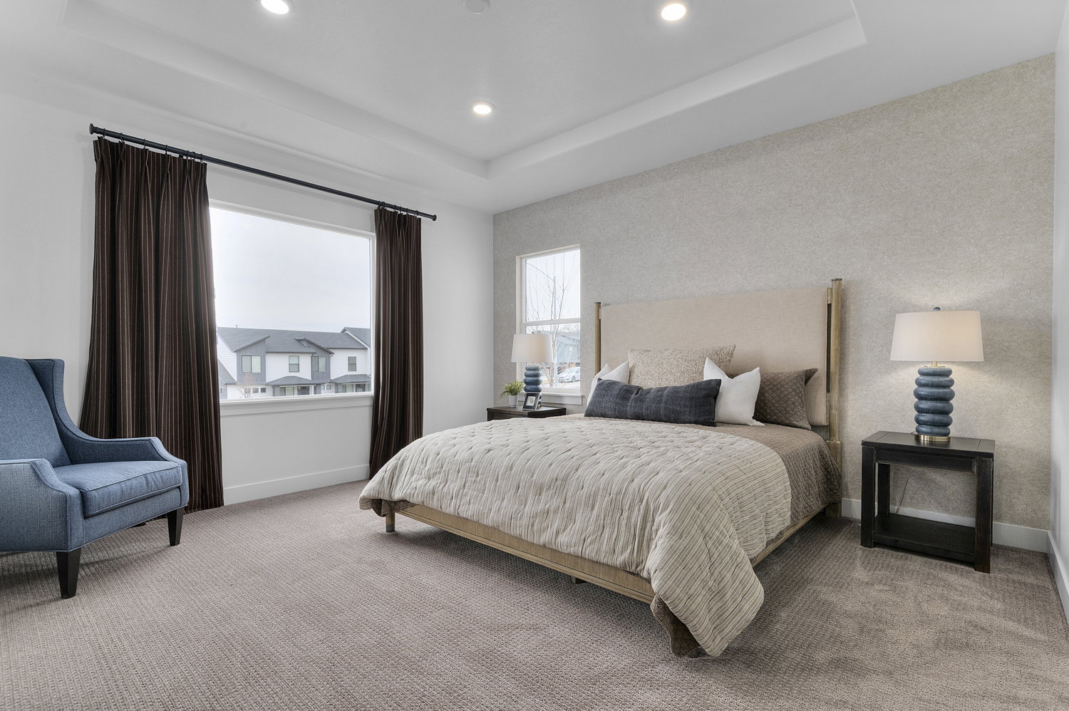 Carpeted interior room featuring a tray ceiling with recessed lighting, large windows with dark drapery, and a textured accent wall