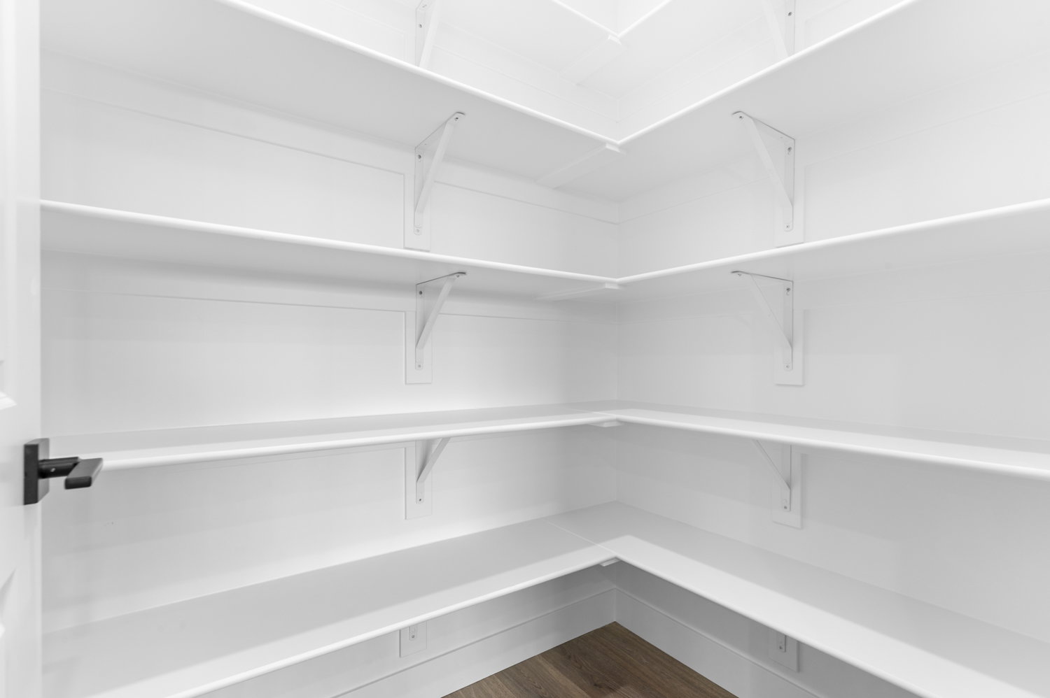 Walk-in pantry featuring white shelving, white walls, and wood-finish flooring