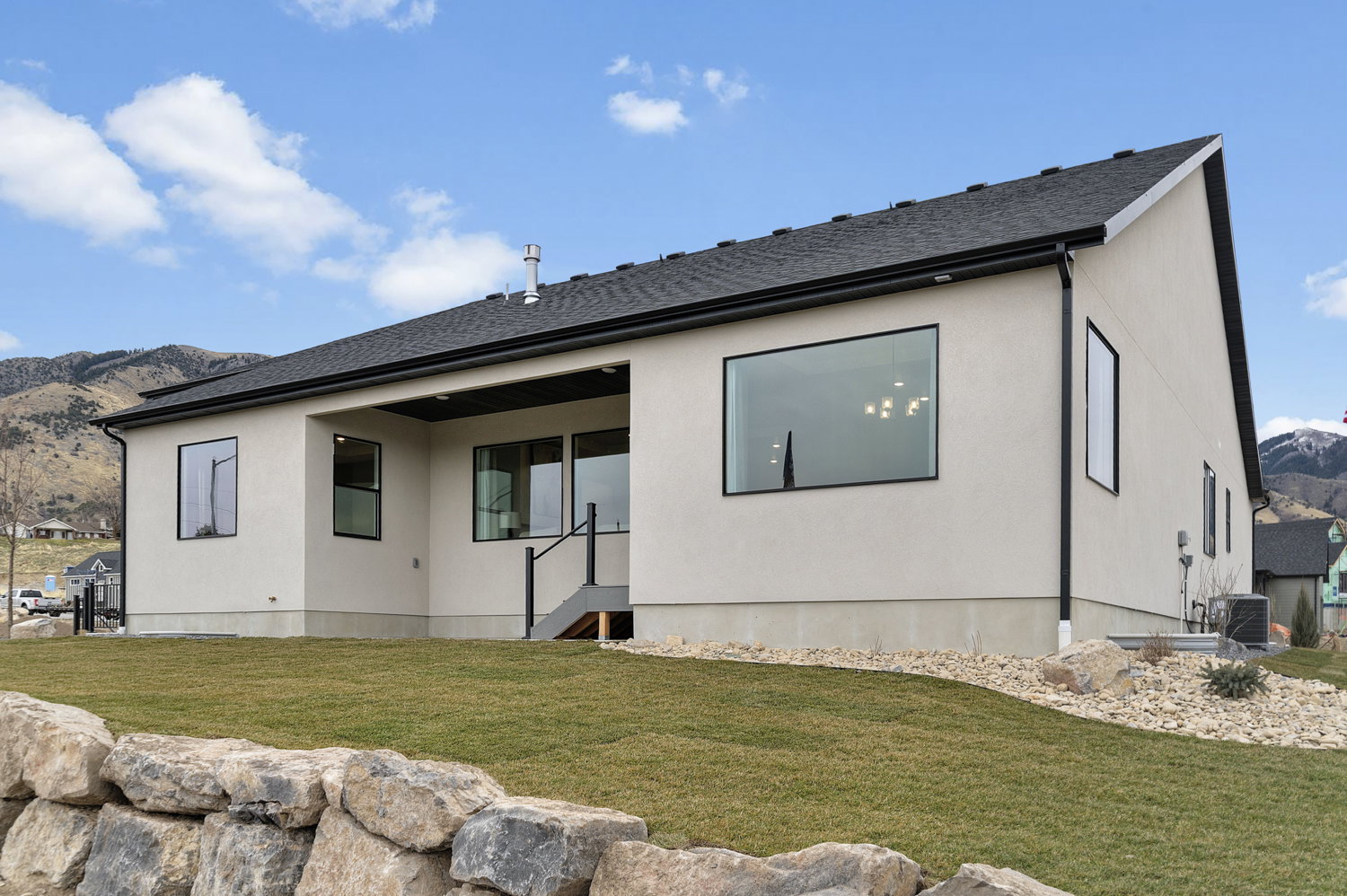 Modern stucco exterior with black-framed windows, a covered patio area, and a dark shingle roof