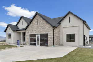 Contemporary exterior featuring a stone and stucco facade, dark-framed windows, a prominent gable roofline, and a concrete driveway