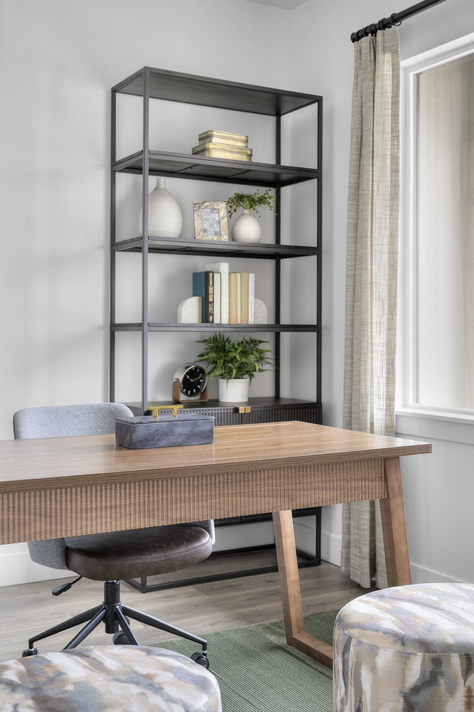 Dedicated workspace featuring a large window, wood-finish flooring, a contemporary metal-frame shelving unit, and a built-in desk with fluted detailing