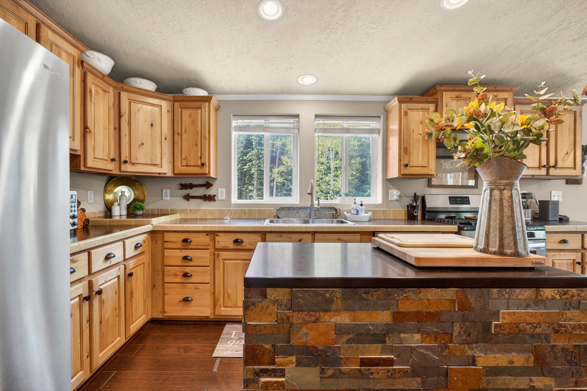 Kitchen featuring a stone-clad island, stainless steel refrigerator, and wood cabinetry