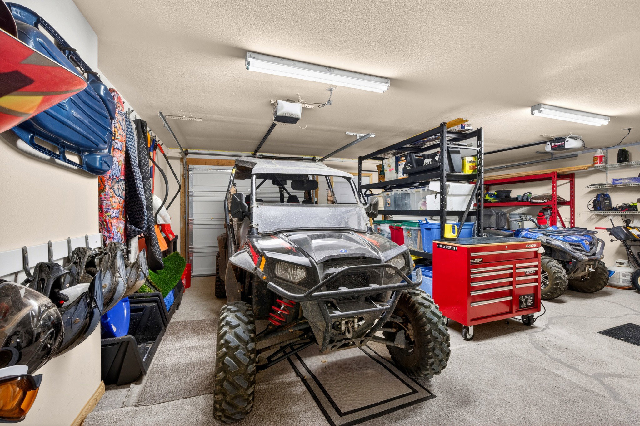 Attached garage with overhead fluorescent lighting, durable concrete flooring, and built-in wall-mounted storage racks