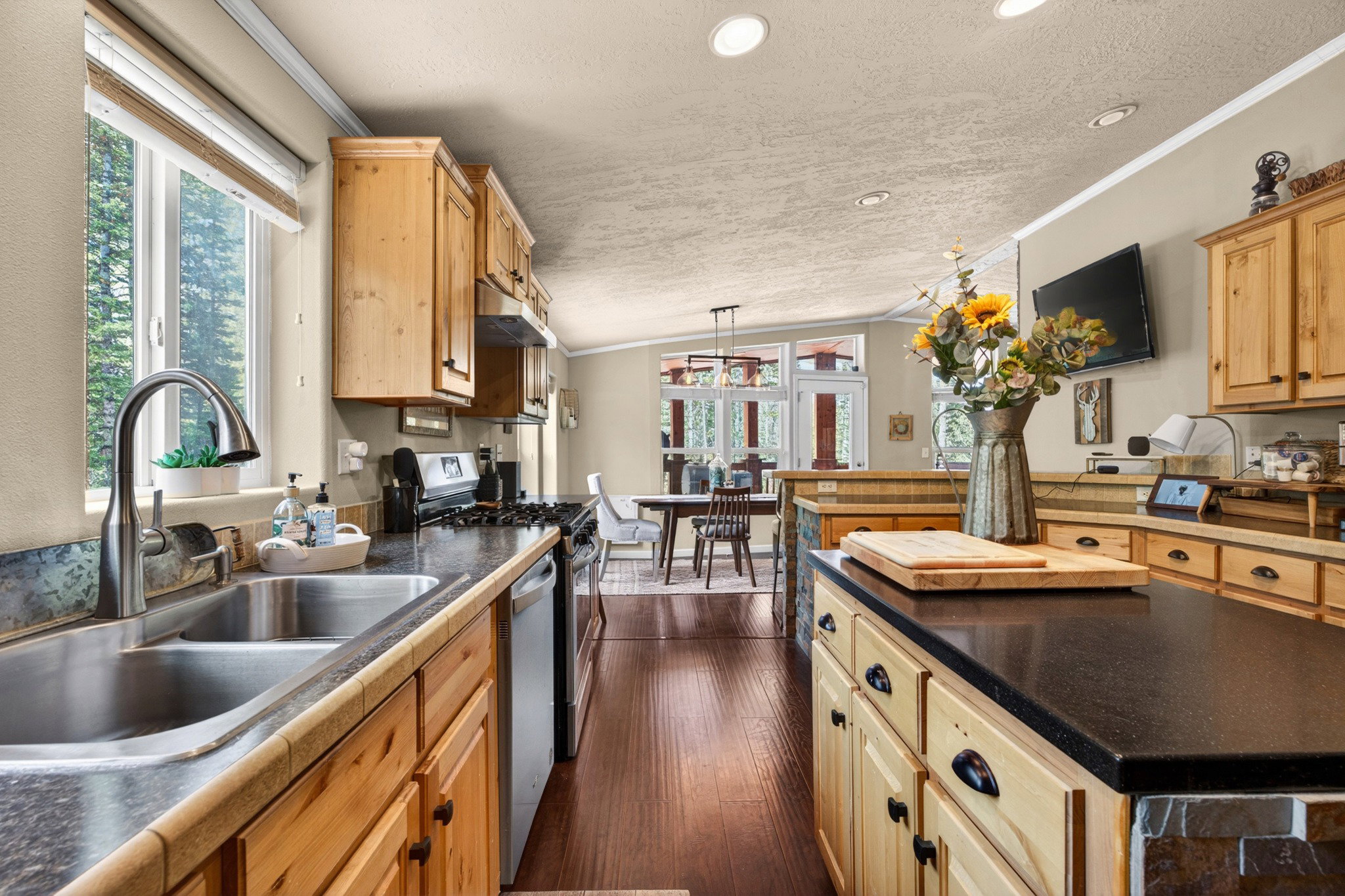 Kitchen featuring wood cabinetry, dark countertops, a stainless steel double basin sink, and a four-burner range with a coordinating hood