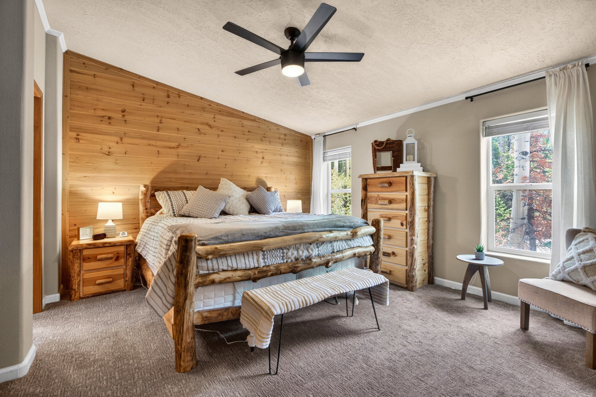 Angled wood-paneled accent wall, neutral wall paint, two double-hung windows, ceiling fan with integrated lighting, and textured carpet flooring