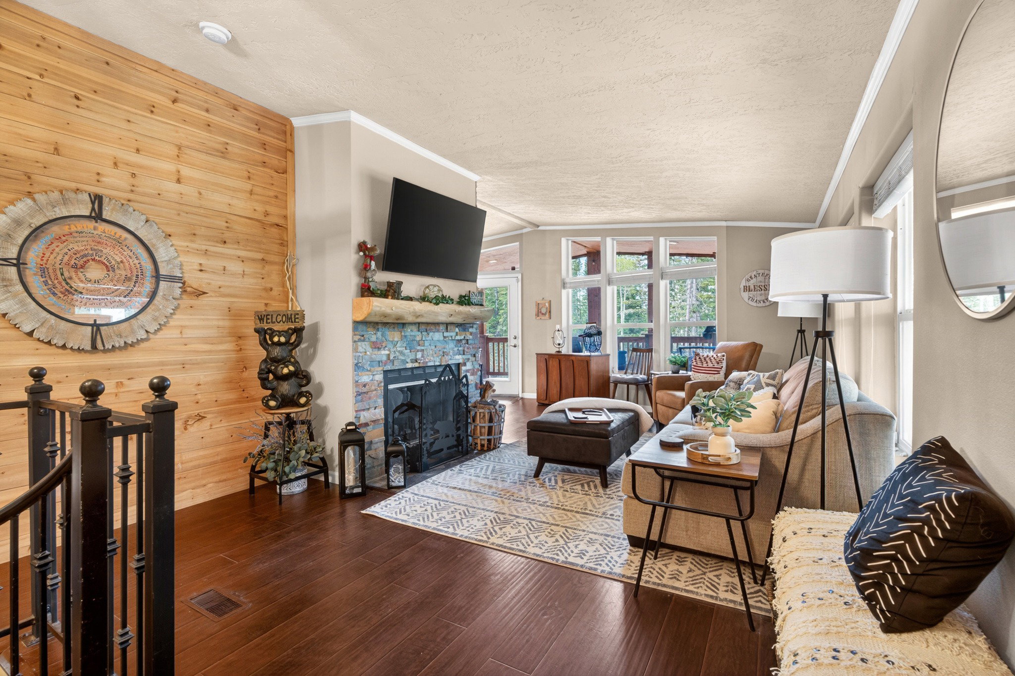 Living area featuring a stone fireplace with a wood mantle, wood-finish flooring, a natural wood accent wall, and large windows