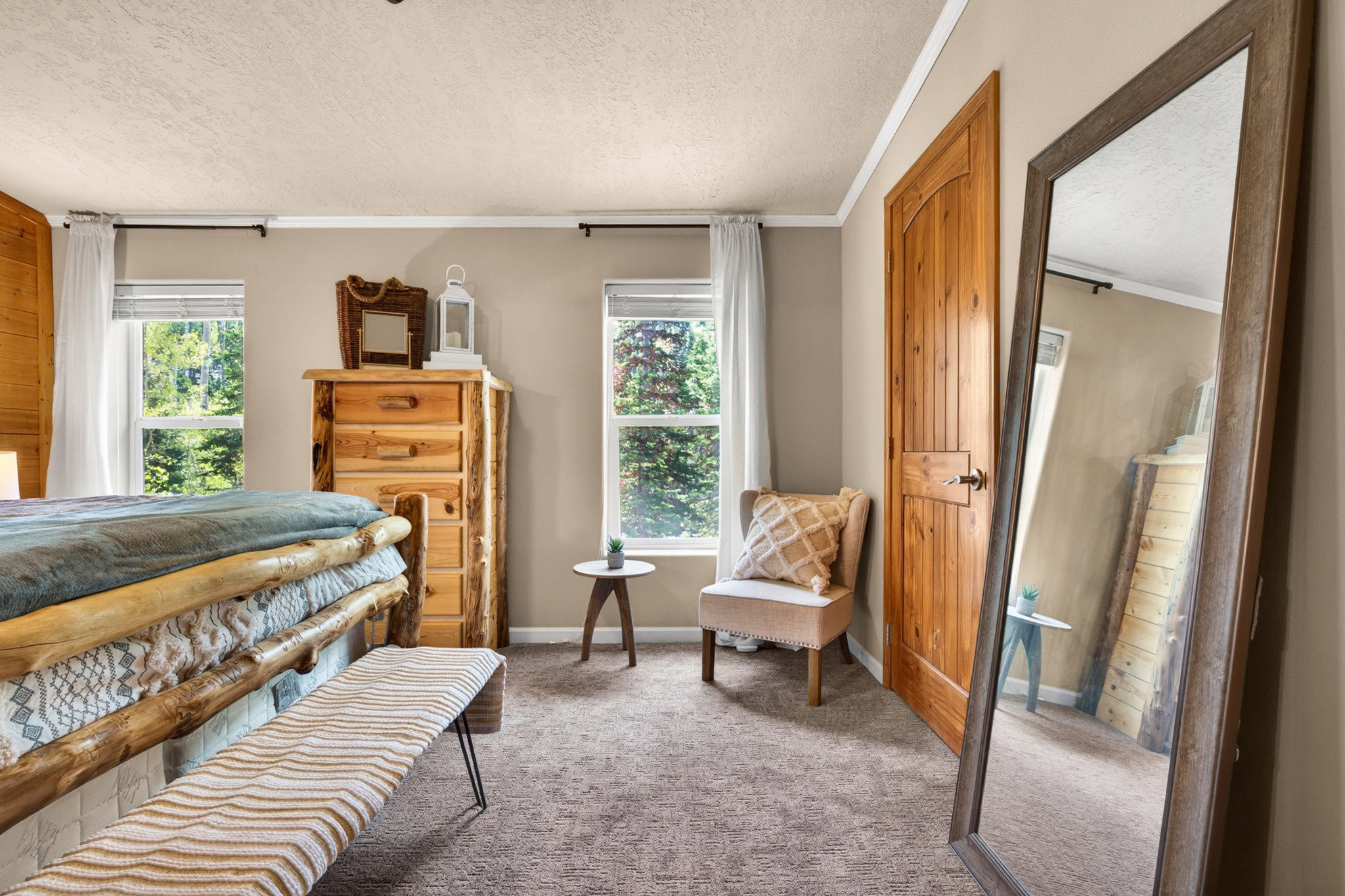Bedroom featuring light neutral wall paint, two windows with white blinds, wood-finish interior door, and textured carpeting