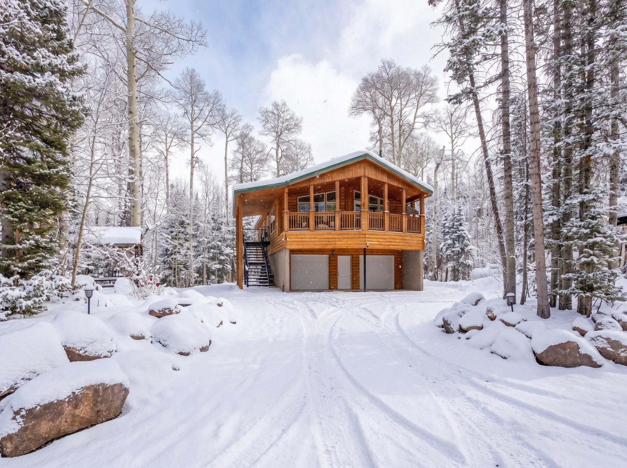 Wood-sided cabin-style residence featuring a covered upper-level deck, ground-level two-car garage, and an exterior staircase