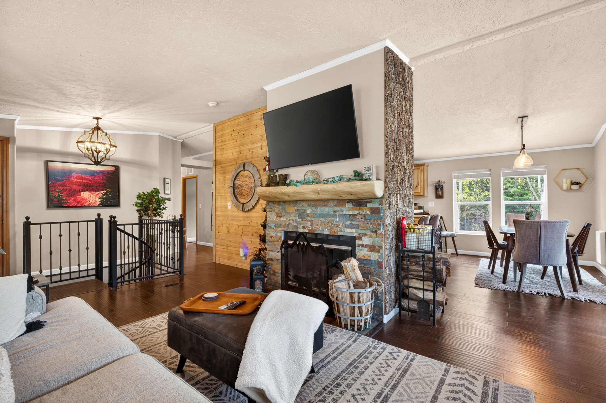 Living area featuring a stone-clad fireplace with a log mantel, rich wood-finish flooring, and a decorative wood-paneled accent wall