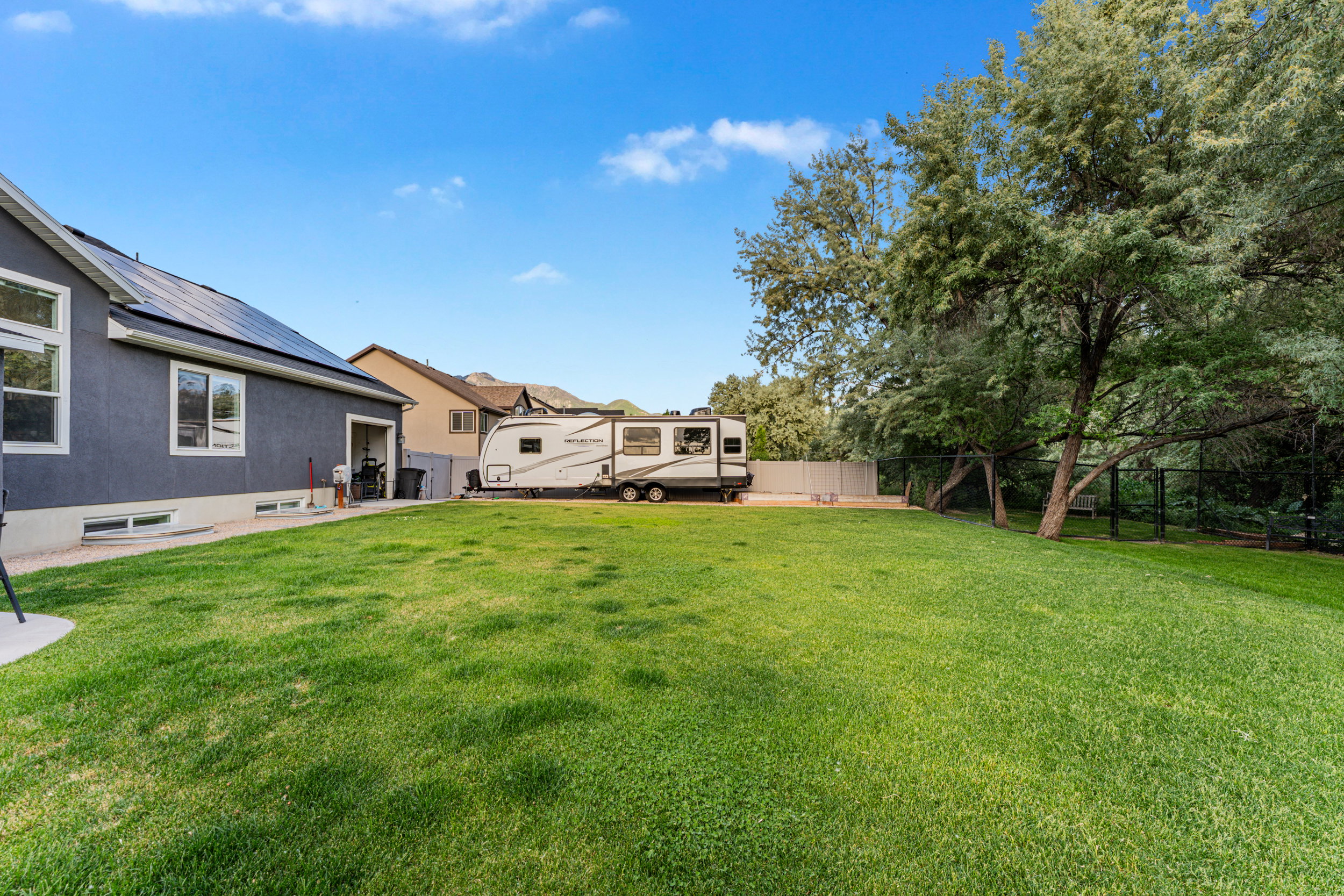 Expansive grassy yard with mature trees and a dark gray stucco exterior