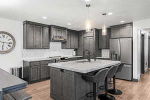 Kitchen featuring a center island with seating, pendant lighting, stainless steel appliances, grey cabinetry, and wood-finish flooring