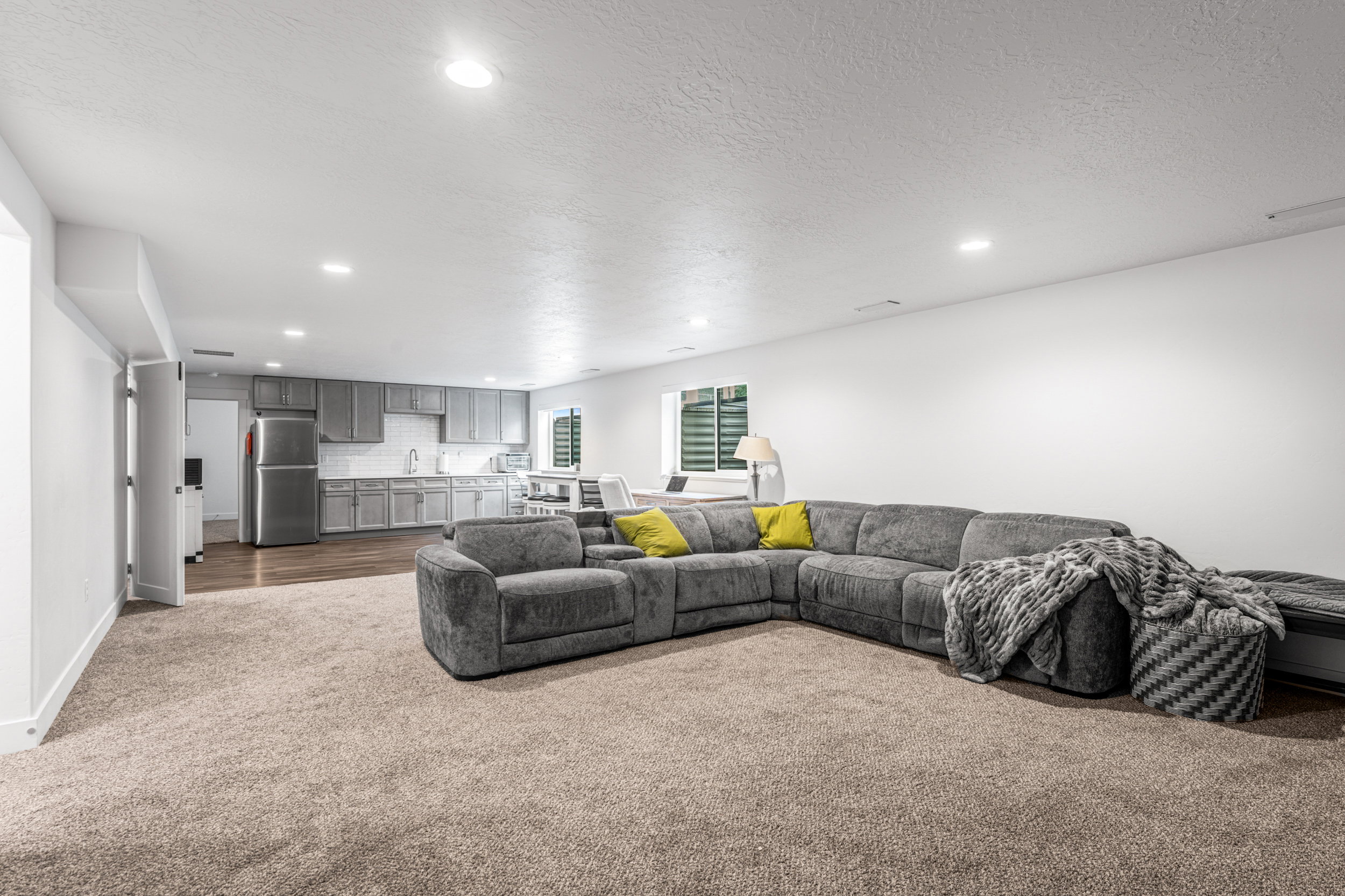 Open-concept room featuring recessed lighting, plush carpeting, a kitchen area with gray cabinetry and stainless steel appliances, and wood-finish flooring