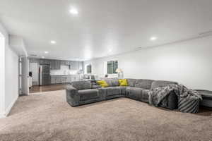 Open-concept room featuring recessed lighting, plush carpeting, a kitchen area with gray cabinetry and stainless steel appliances, and wood-finish flooring