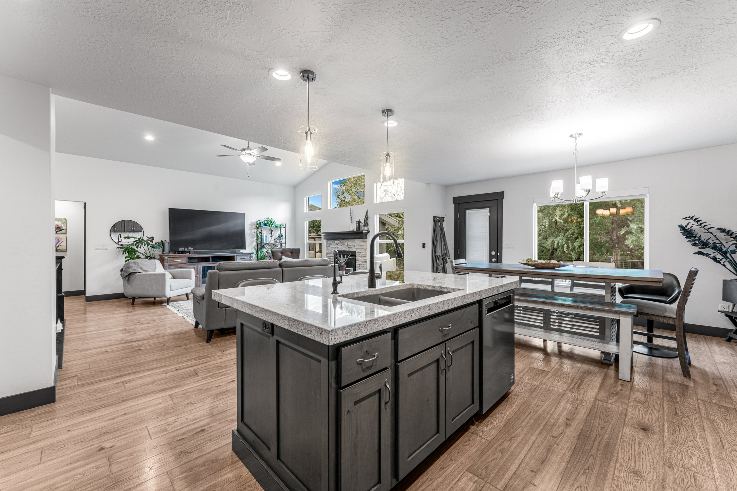 Open-concept interior featuring wood-finish flooring, a kitchen island with stone countertops and an undermount sink, recessed lighting, and vaulted ceilings