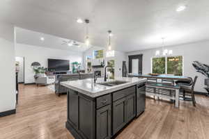 Open-concept interior featuring wood-finish flooring, a kitchen island with stone countertops and an undermount sink, recessed lighting, and vaulted ceilings